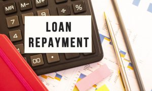 The words ‘Loan Repayment’ over a calculator on an office desk