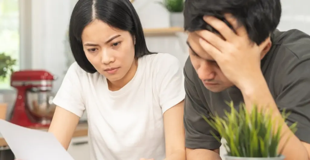Stressed young couple calculating various debts, wondering if others can take a legal loan in Singapore on their behalf